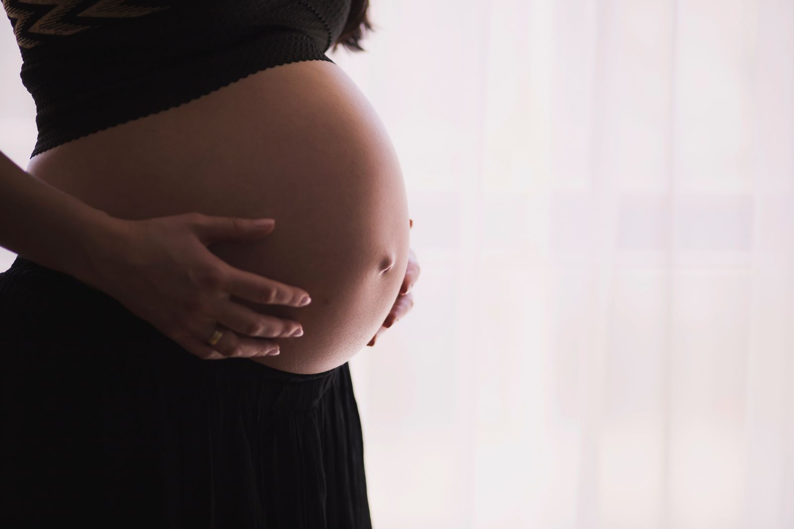 A pregnant woman in silhouette holding her belly in front of a bright window.