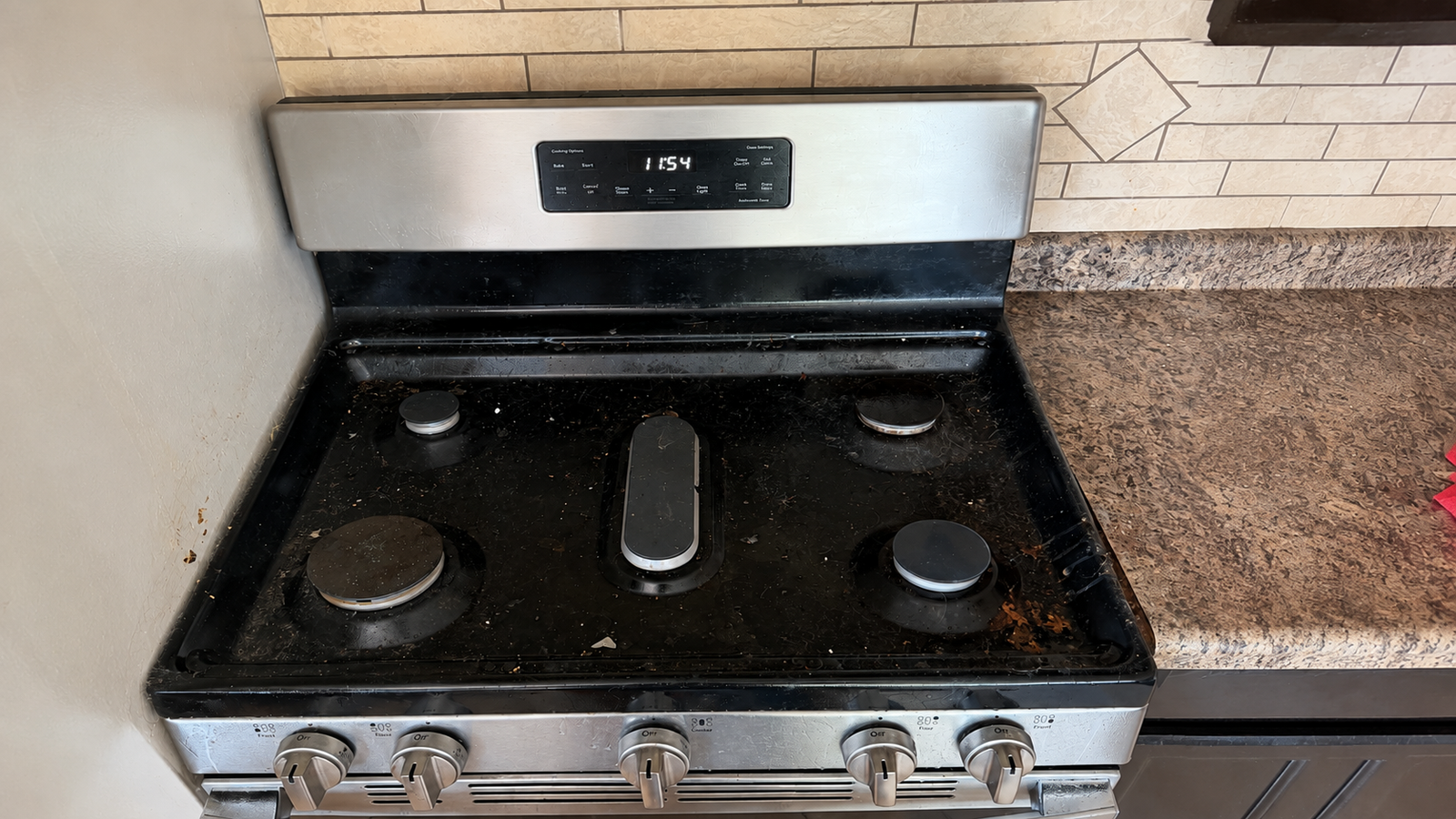 A stainless steel five-burner gas stove with visible grease and grime built up on the cooking surface.