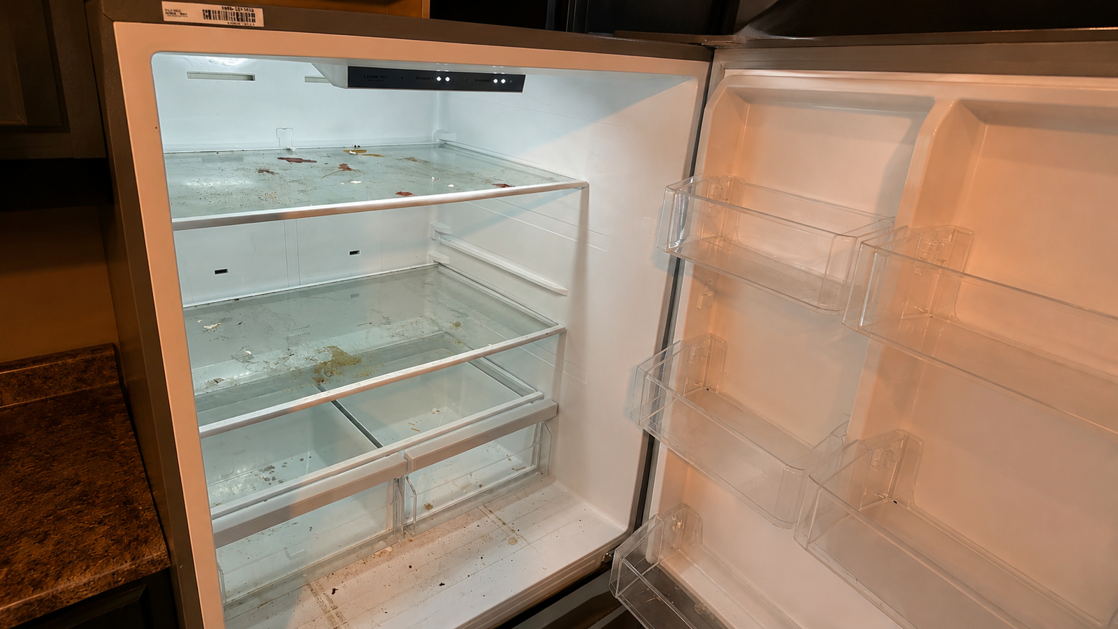 An open refrigerator interior with dust, stains and residue on the shelves.