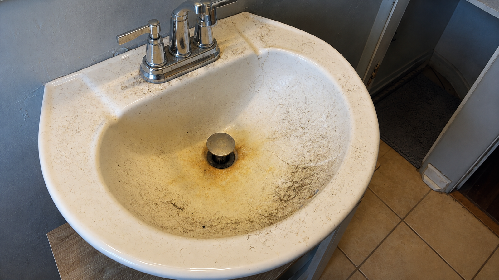 A pedestal sink with visible stains and discolouration before cleaning.