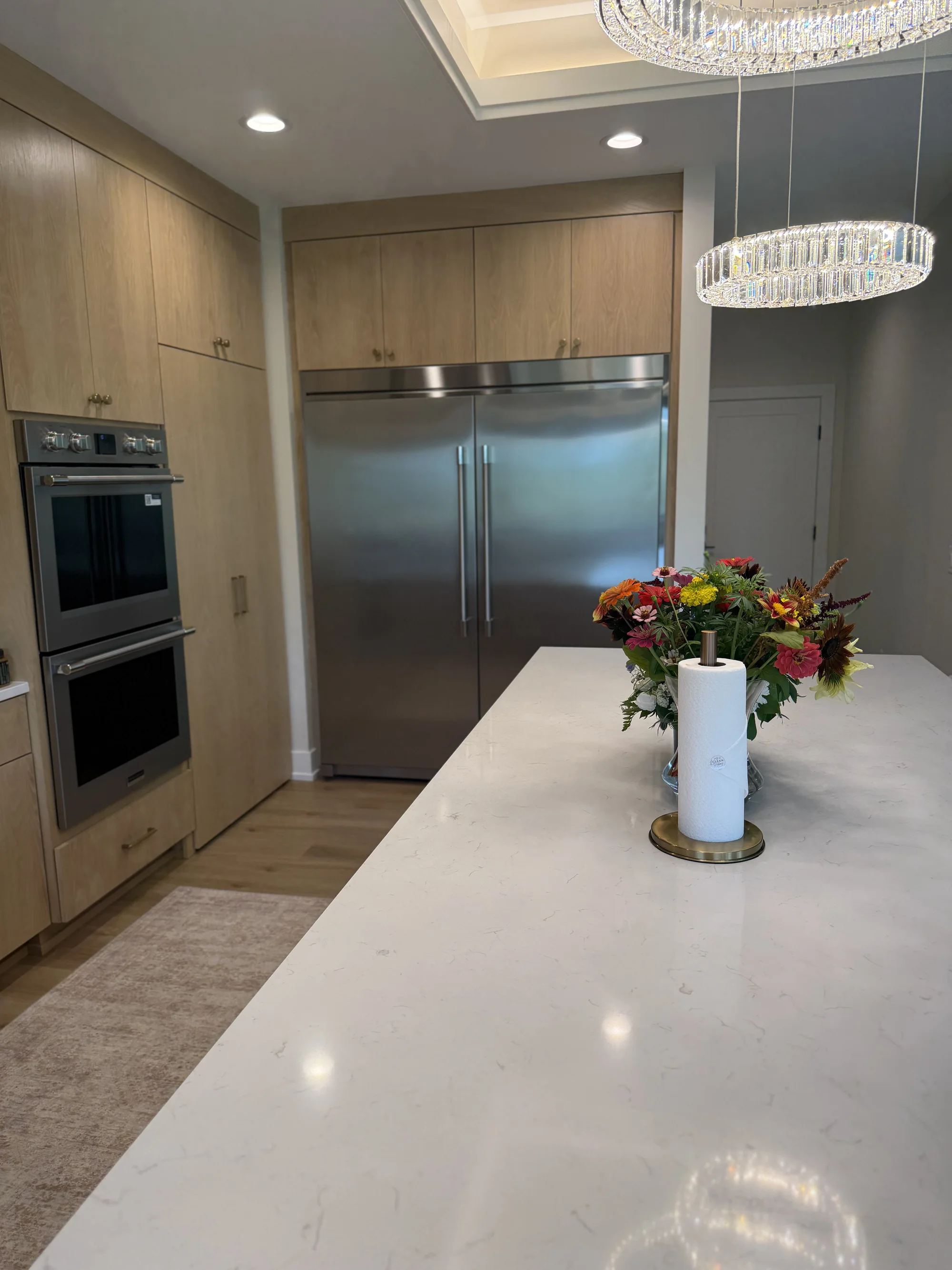 A bright, upscale kitchen with a stainless refrigerator, a marble island, and fresh flowers beside a Clean Vibes branded paper towel roll.